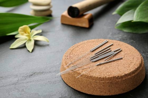 Cork coaster with acupuncture needles on black table. Space for