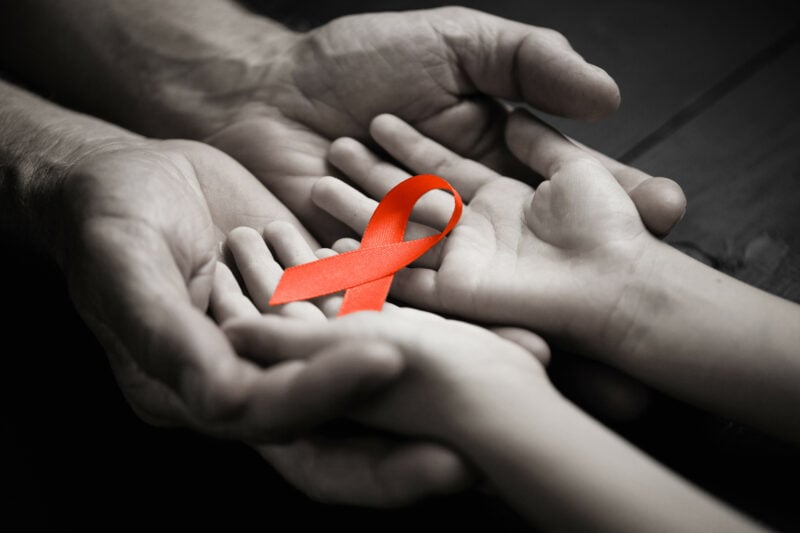 Aid Red Ribbon In Hand On A Black Wooden Background.black And Wh