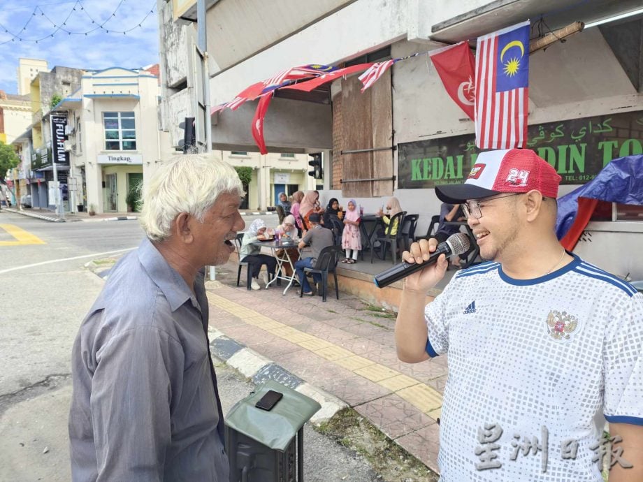 东：马来西亚日的哥市街头，一名驻唱的白发老伯在茶餐室前面开嗓献艺，他应客人要求唱了一首生日歌，仿佛也在歌唱自己的乐天和家国的欢腾，令人动容。