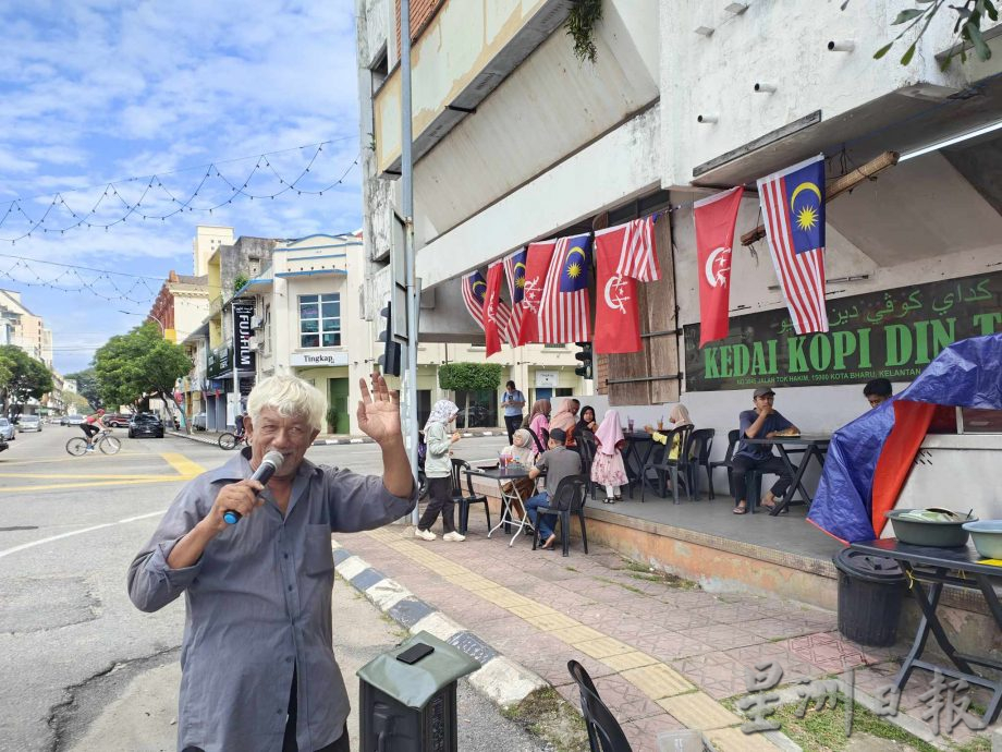 东：马来西亚日的哥市街头，一名驻唱的白发老伯在茶餐室前面开嗓献艺，他应客人要求唱了一首生日歌，仿佛也在歌唱自己的乐天和家国的欢腾，令人动容。